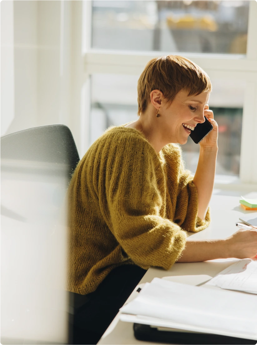 A woman in a yellow sweater talks on the phone and laughs.