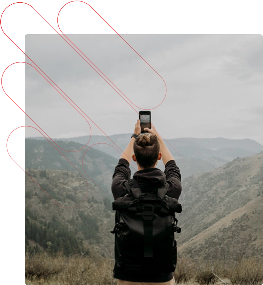 A man stands in front of an expansive landscape, holding up a phone.