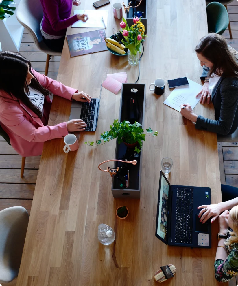 Overhead shot of an office table with at least 4 people working at it.
