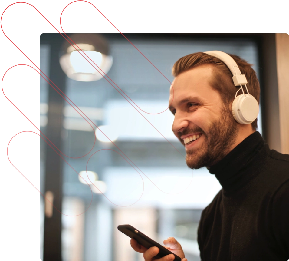 A man in a black turtleneck smiles. He is holding a phone and wearing white headphones.