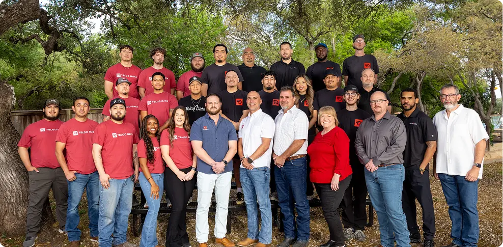 Photo of the entire Telco Data team. They are outside and wearing matching black and grey shirts.